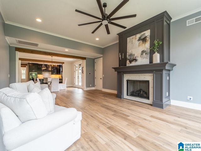 living room featuring ceiling fan with notable chandelier, a premium fireplace, ornamental molding, and light hardwood / wood-style flooring