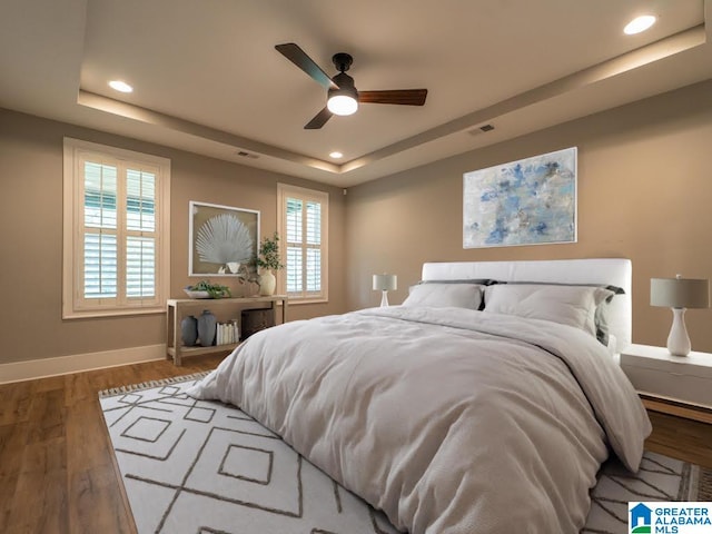 bedroom with a tray ceiling, multiple windows, ceiling fan, and dark hardwood / wood-style floors