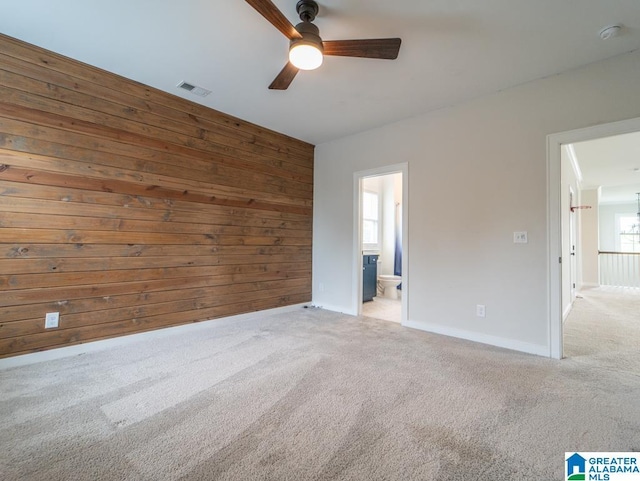 unfurnished room with light carpet, plenty of natural light, ceiling fan, and wooden walls