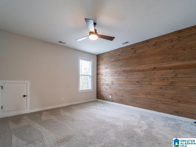 unfurnished room featuring carpet, ceiling fan, and wood walls