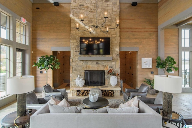 living room with a notable chandelier, wood walls, a stone fireplace, and a towering ceiling