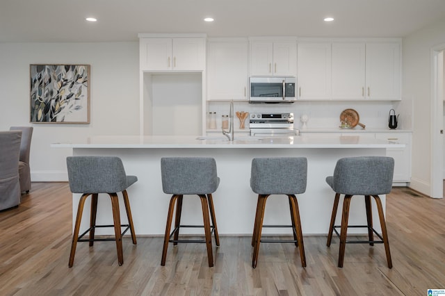 kitchen featuring sink, appliances with stainless steel finishes, a large island, a kitchen bar, and white cabinetry