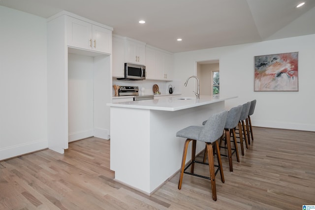 kitchen with appliances with stainless steel finishes, sink, light hardwood / wood-style floors, white cabinetry, and a breakfast bar area