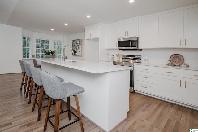 kitchen featuring appliances with stainless steel finishes, light wood-type flooring, sink, a center island with sink, and white cabinets