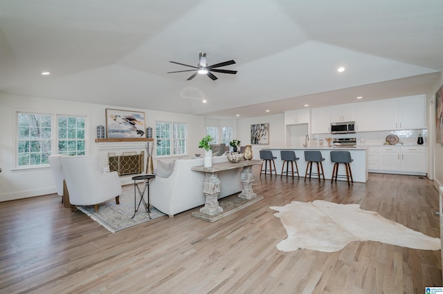 living room featuring ceiling fan, light hardwood / wood-style floors, lofted ceiling, and sink