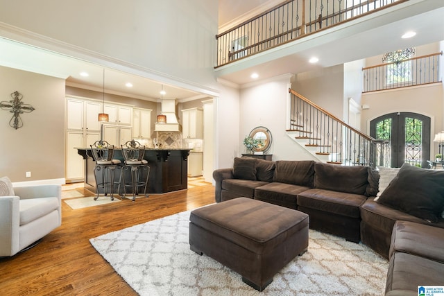 living room with french doors, a towering ceiling, ornamental molding, and light wood-type flooring