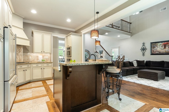 kitchen with light stone countertops, a kitchen breakfast bar, a kitchen island with sink, decorative light fixtures, and built in fridge