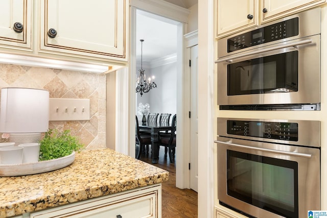 kitchen featuring decorative backsplash, light stone counters, double oven, and a notable chandelier