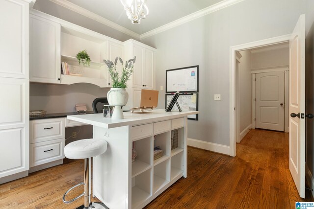 kitchen featuring dark wood-type flooring, white cabinets, hanging light fixtures, built in desk, and a breakfast bar area