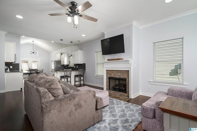 living room with dark hardwood / wood-style flooring, ceiling fan with notable chandelier, vaulted ceiling, crown molding, and a stone fireplace