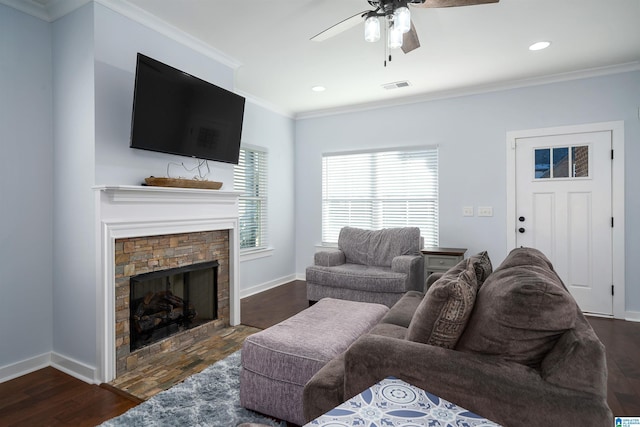 living room featuring a stone fireplace, ceiling fan, dark wood-type flooring, and crown molding