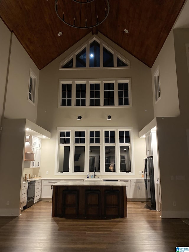 kitchen with white cabinetry, black fridge, wooden ceiling, light wood-type flooring, and wall chimney exhaust hood