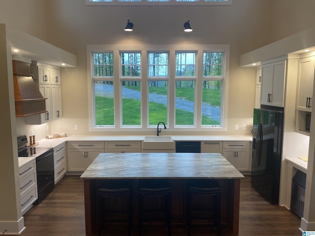 kitchen with sink, a breakfast bar, black appliances, white cabinets, and a kitchen island