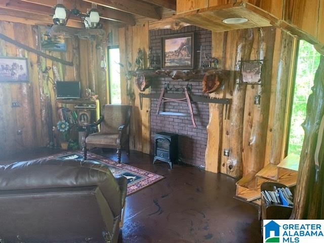 living room featuring beam ceiling, a wood stove, and wooden walls