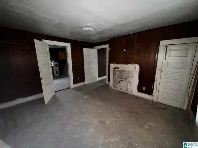 unfurnished bedroom featuring concrete floors, water heater, and wood walls