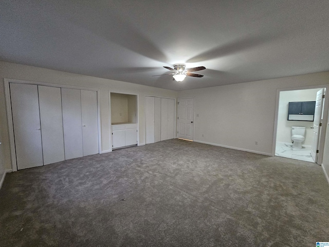 unfurnished bedroom with carpet floors, ensuite bathroom, ceiling fan, and two closets