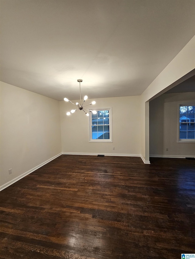 spare room with an inviting chandelier and dark wood-type flooring