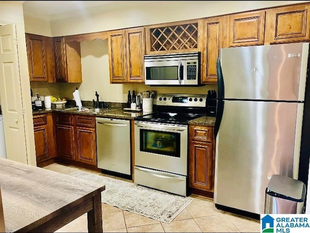 kitchen with light tile patterned flooring, dark stone countertops, sink, and appliances with stainless steel finishes