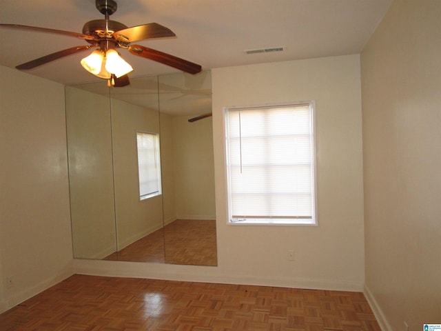 empty room featuring ceiling fan, a healthy amount of sunlight, and parquet flooring