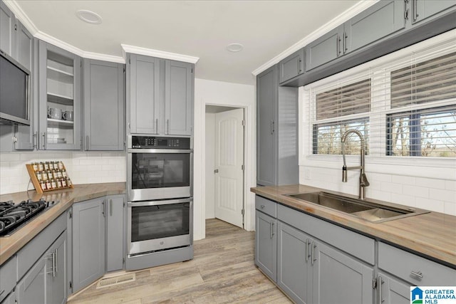 kitchen with gray cabinetry, appliances with stainless steel finishes, butcher block counters, and sink