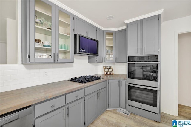 kitchen with stainless steel appliances, butcher block countertops, light hardwood / wood-style floors, gray cabinets, and decorative backsplash