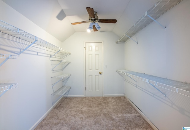 spacious closet with ceiling fan, light colored carpet, and vaulted ceiling