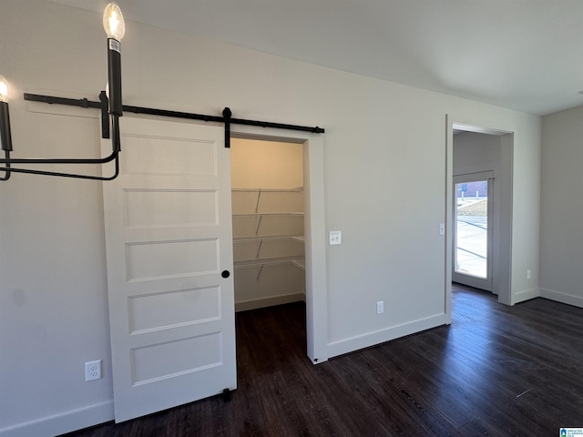 unfurnished bedroom featuring a walk in closet, a closet, dark hardwood / wood-style flooring, and a barn door