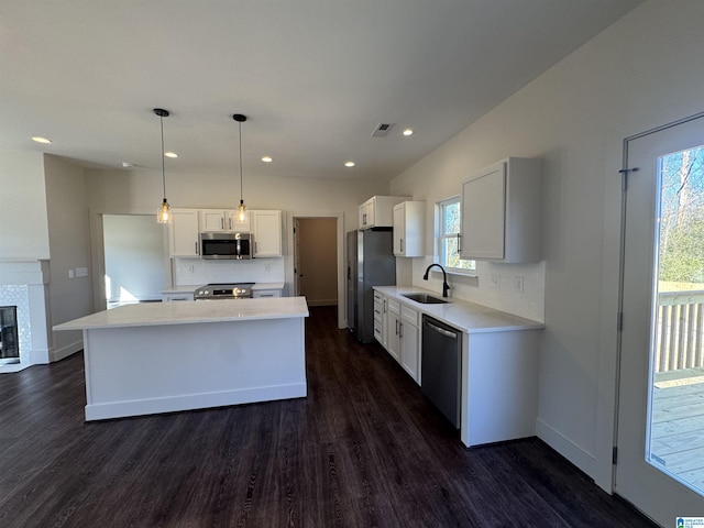 kitchen with stainless steel appliances, sink, decorative light fixtures, a center island, and white cabinetry