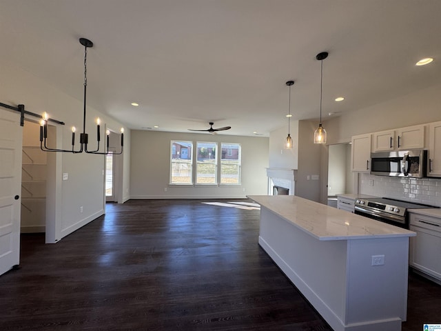 kitchen with light stone countertops, hanging light fixtures, a barn door, white cabinets, and appliances with stainless steel finishes