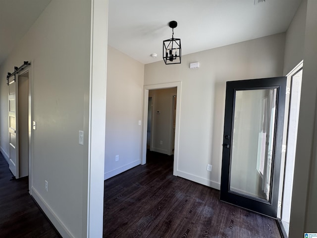 hall with a barn door, an inviting chandelier, and dark wood-type flooring