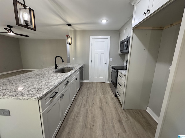 kitchen with appliances with stainless steel finishes, white cabinetry, sink, hanging light fixtures, and light stone counters