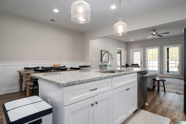 kitchen featuring stainless steel dishwasher, a kitchen island with sink, sink, white cabinets, and hanging light fixtures