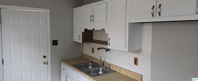 kitchen with backsplash, white cabinetry, and sink