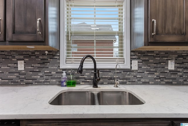 kitchen with dark brown cabinets, light stone countertops, tasteful backsplash, and a sink