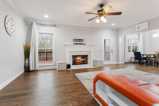 living area with a ceiling fan, wood finished floors, baseboards, a high end fireplace, and crown molding