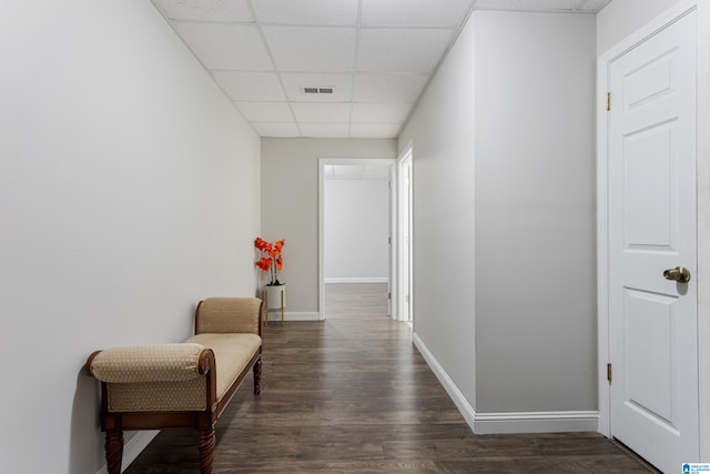 hall featuring dark wood-type flooring, a paneled ceiling, baseboards, and visible vents