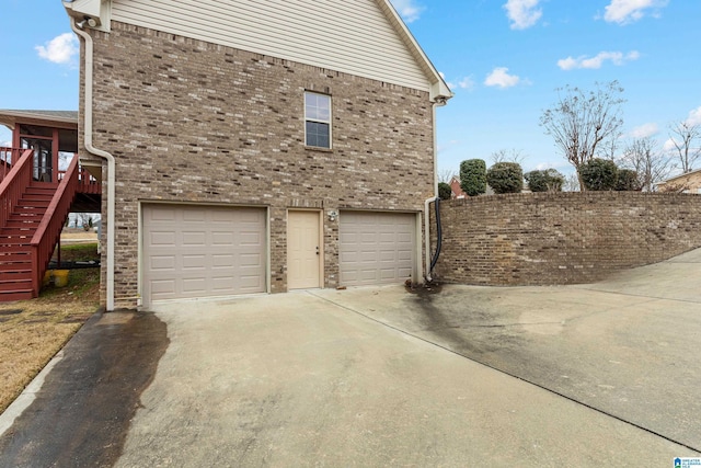 view of side of property featuring a garage, driveway, brick siding, and stairs