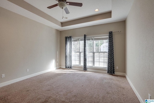 carpeted empty room featuring ceiling fan and a raised ceiling