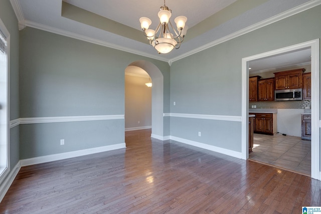 spare room with a notable chandelier, a raised ceiling, wood-type flooring, and ornamental molding