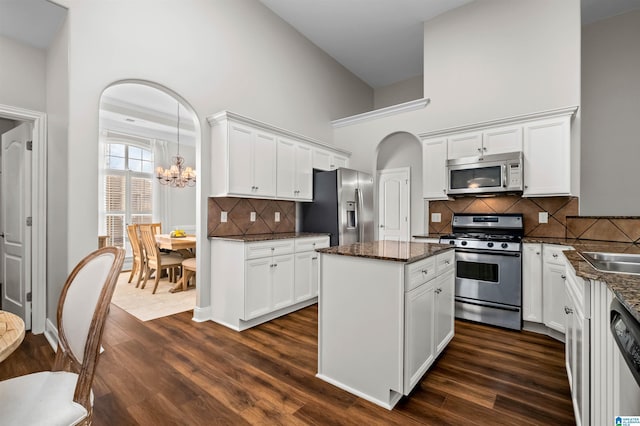 kitchen featuring white cabinetry, stainless steel appliances, a notable chandelier, a towering ceiling, and decorative backsplash