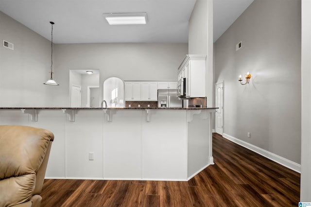 kitchen with white cabinets, hanging light fixtures, appliances with stainless steel finishes, dark hardwood / wood-style flooring, and a breakfast bar area