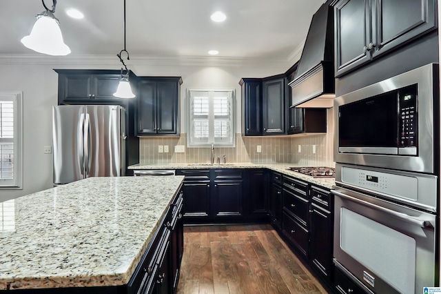 kitchen with custom exhaust hood, stainless steel appliances, light stone countertops, sink, and decorative light fixtures