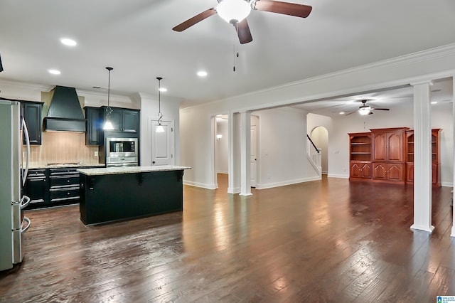 kitchen featuring stainless steel appliances, premium range hood, pendant lighting, decorative backsplash, and a kitchen island