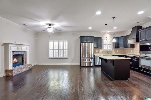 kitchen featuring light stone counters, a center island, hanging light fixtures, custom range hood, and appliances with stainless steel finishes