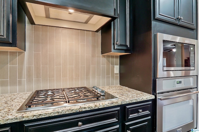 kitchen featuring light stone counters, stainless steel appliances, ventilation hood, and tasteful backsplash