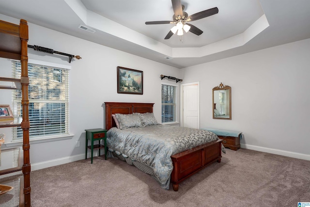 carpeted bedroom featuring a tray ceiling and ceiling fan