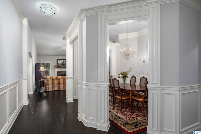 hallway featuring dark hardwood / wood-style flooring, ornate columns, crown molding, and a chandelier