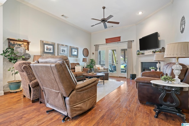 living room with a high ceiling, crown molding, ceiling fan, a fireplace, and wood-type flooring