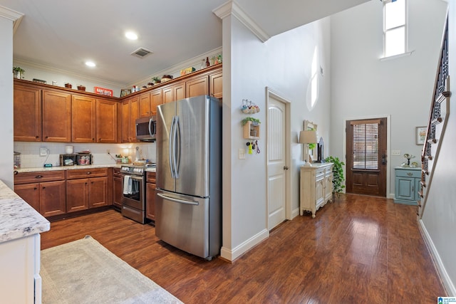 kitchen featuring dark wood-type flooring, light stone countertops, ornamental molding, appliances with stainless steel finishes, and tasteful backsplash