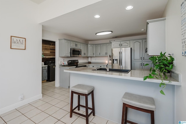 kitchen featuring kitchen peninsula, appliances with stainless steel finishes, a kitchen breakfast bar, sink, and gray cabinets